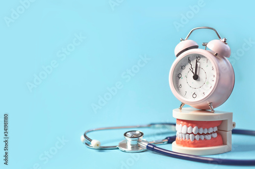 White teeth model with alarm clock on blue background. me to dental health. Dentist day concept. copy space for text.