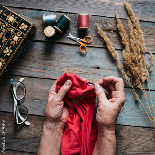 Female hands sewing on wooden table, scissors, casket, thread, glasses