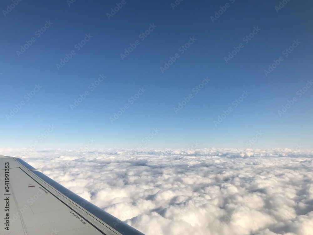 High up in the stratosphere, close to heaven: Above the white clouds on a scenic journey in an airplane flight of a vacation journey seeing the aircraft wing gliding over the bright cloudscape