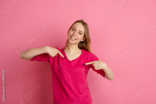 Pointing at herself. Caucasian young woman's portrait isolated on pink studio background, monochrome. Beautiful female model. Concept of human emotions, facial expression, sales, ad, trendy. © master1305