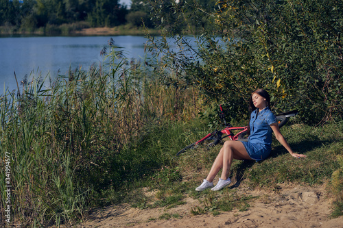 Weekend, outdoor recreation. The girl, leaning on her hands, sits by the lake with reeds. Side view.