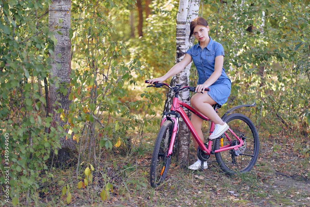 Naklejka premium A student sitting in a blue dress on a female bike on nature in a birch forest.