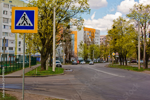 Cars driving along a street with traffic signs between trees and houses in the evening
