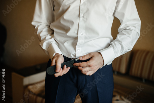 A stylish man puts on a leather belt close-up. Fashion