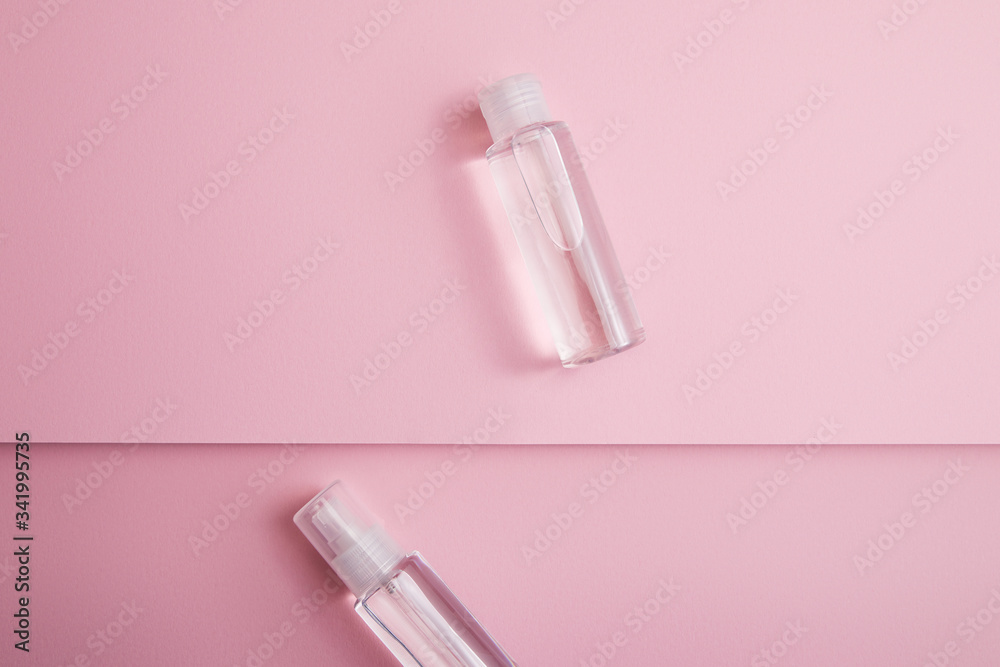 Top view of transparent hand sanitizer in bottle and spray with liquid on pink background Top view of transparent hand sanitizer in bottle and spray with liquid on pink background
