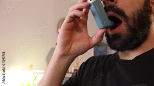 Young man blue shirt using blue asthma inhaler for relief asthma attack. Pharmaceutical products is used to prevent and treat wheezing and shortness of breath caused asth photo