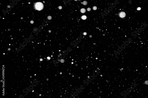 Small white snowflakes fall from the night sky. Snowfall in winter on a black background.