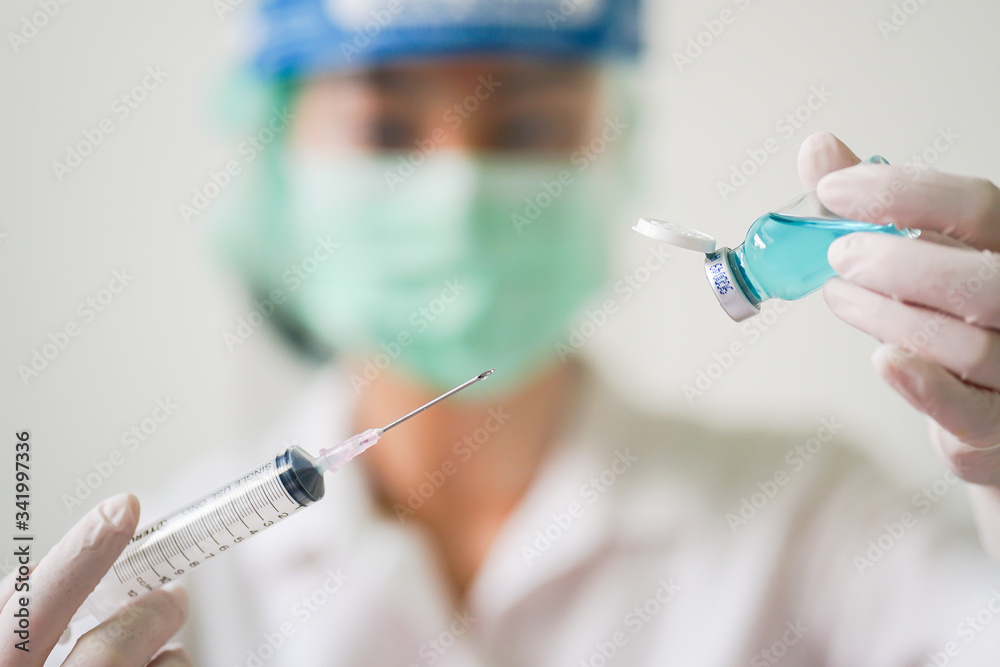 Close up medical doctor wearing face shield, medical mask and medical grove. She holding draw syringe and bottle with Coronavirus vaccine for 2019-nCoV COVID virus. Close up medical doctor wearing face shield, medical mask and medical grove. She holding draw syringe and bottle with Coronavirus vaccine for 2019-nCoV COVID virus.