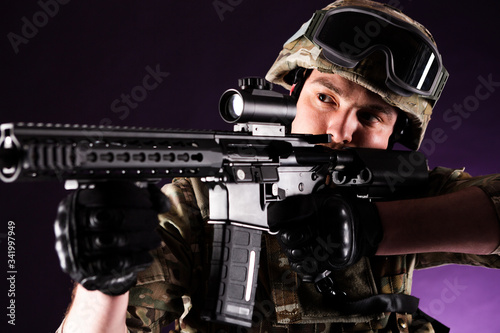 Soldier with gun is looking through the scope on violet background. Concept of war. Veterans, comrades, soldiers. Man in uniform. photo