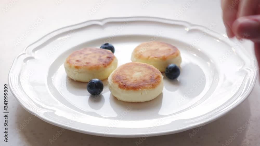 Woman puts blueberries on the plate with cheese pancakes Woman puts blueberries on the plate with cheese pancakes