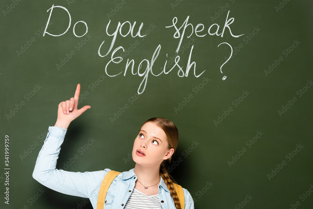 girl with backpack pointing at chalkboard with do you speak English lettering girl with backpack pointing at chalkboard with do you speak English lettering
