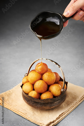Loukoumades, luqaimat or lokma with syrup in vintage metal cup on grey concrete background. Loukoumades is eastern cuisine donunts popular during Ramazan. Popular Ramadan Food. Iftar and Suhur sweets. photo