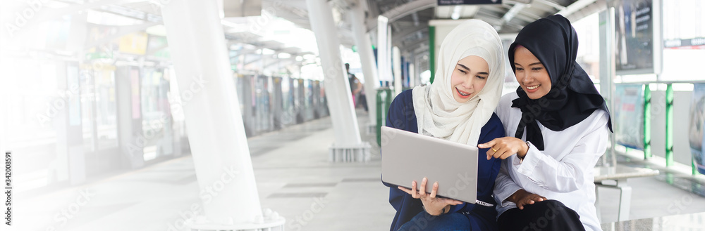 Beautiful asian muslim woman two person working with laptop at electric train station. work at holiday concept.
