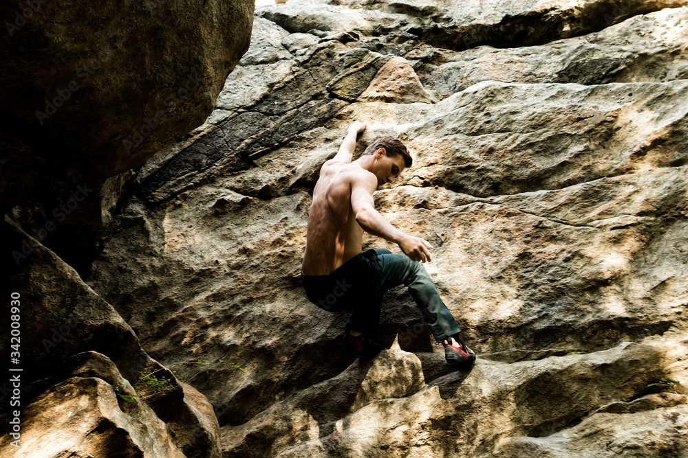 Rock climber climbs bouldering on a cliff on forest. Low angle of strong rock climbing man hanging free on rock with sunflare Rock climber climbs bouldering on a cliff on forest. Low angle of strong rock climbing man hanging free on rock with sunflare