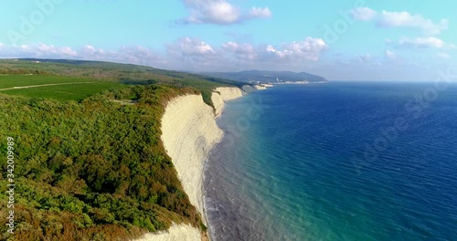 Flying over the black sea coast with big white rocks. At the foot of the rocks is a small pebble beach. On the Bank of the forest. In the background is the resort village of Divnomorskoe. The sea is photo