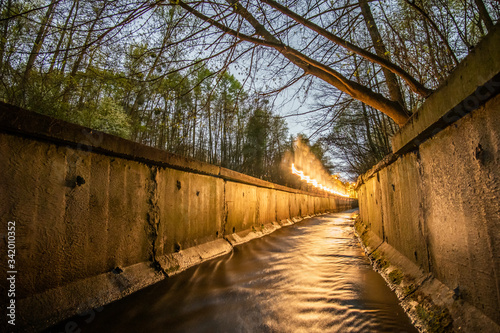 A stream in a concrete ditch or rainwater channel at night in forest with flying lighting warm light  freezelight . Storm drainage in the evening.