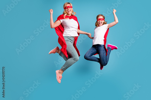 Full length photo of funny mom lady little daughter spend time together superhero win costume competition jump high up wear s-shirts red coat masks isolated blue color background