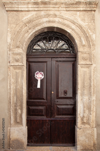 Ancient wooden door of a historic building, with a pink bow that signals the birth of a baby girl © Restuccia Giancarlo
