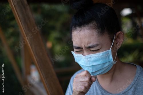 Shot of illness young Asia woman standing to put on a medical mask have coughing in the park at blurred background