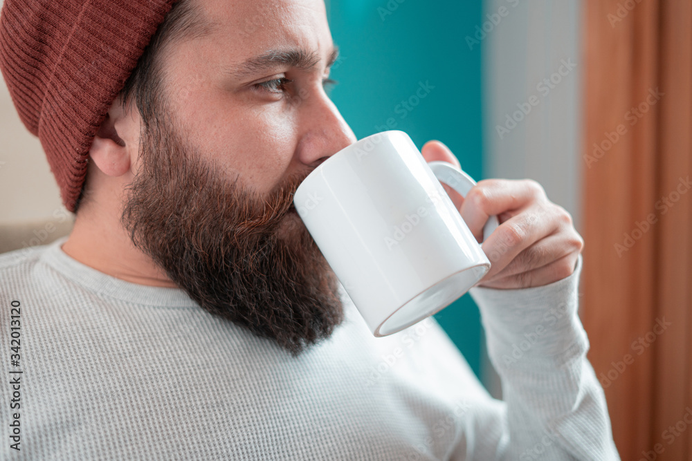 Young designer with hipster beard drinking coffee with an empty mockup cup staring outside Young designer with hipster beard drinking coffee with an empty mockup cup staring outside
