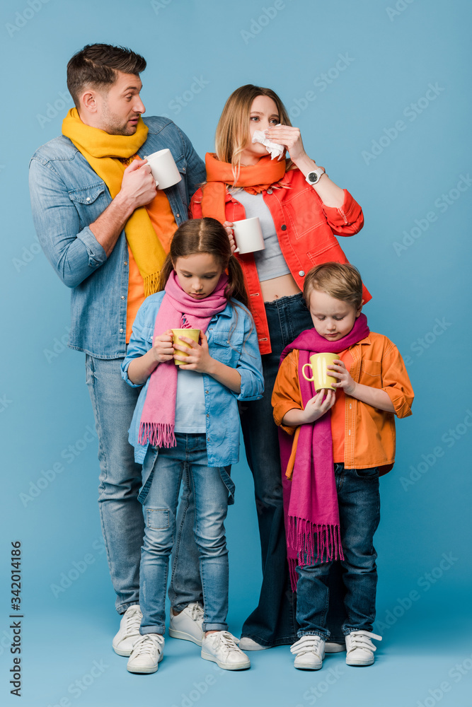 sad ill family with kids in scarves holding cups with hot drinks on blue