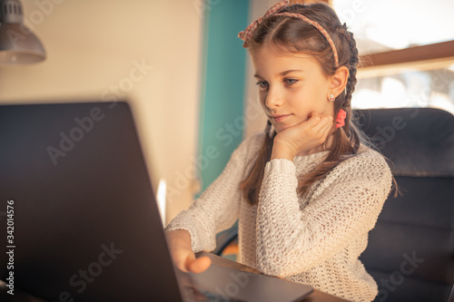 Beautiful 9 year old brunette girl studying from home during coronavirus covid19 quarantine with her laptop