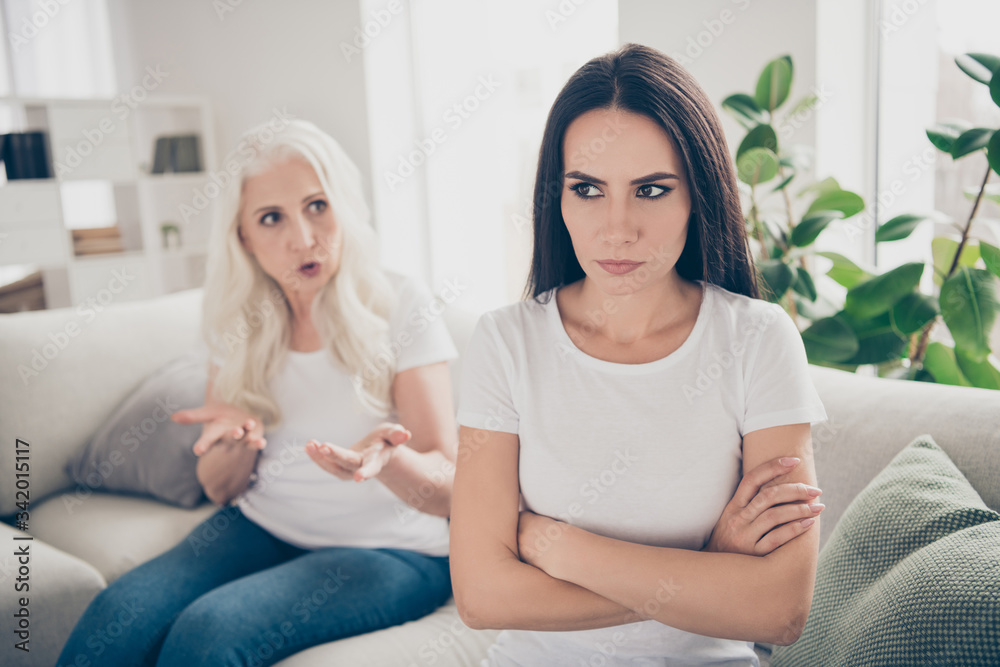 Close-up portrait of two nice attractive depressed women sitting on divan grandma talking claiming problems pretense disagree negative emotion in white light interior house flat apartment indoors Close-up portrait of two nice attractive depressed women sitting on divan grandma talking claiming problems pretense disagree negative emotion in white light interior house flat apartment indoors