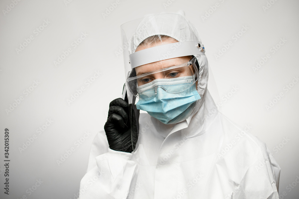 woman in medical protective clothing and black latex glove holds phone near her ear woman in medical protective clothing and black latex glove holds phone near her ear