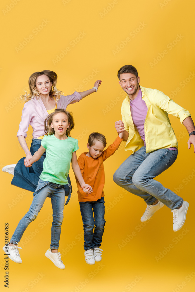 excited family jumping and holding hands on yellow excited family jumping and holding hands on yellow