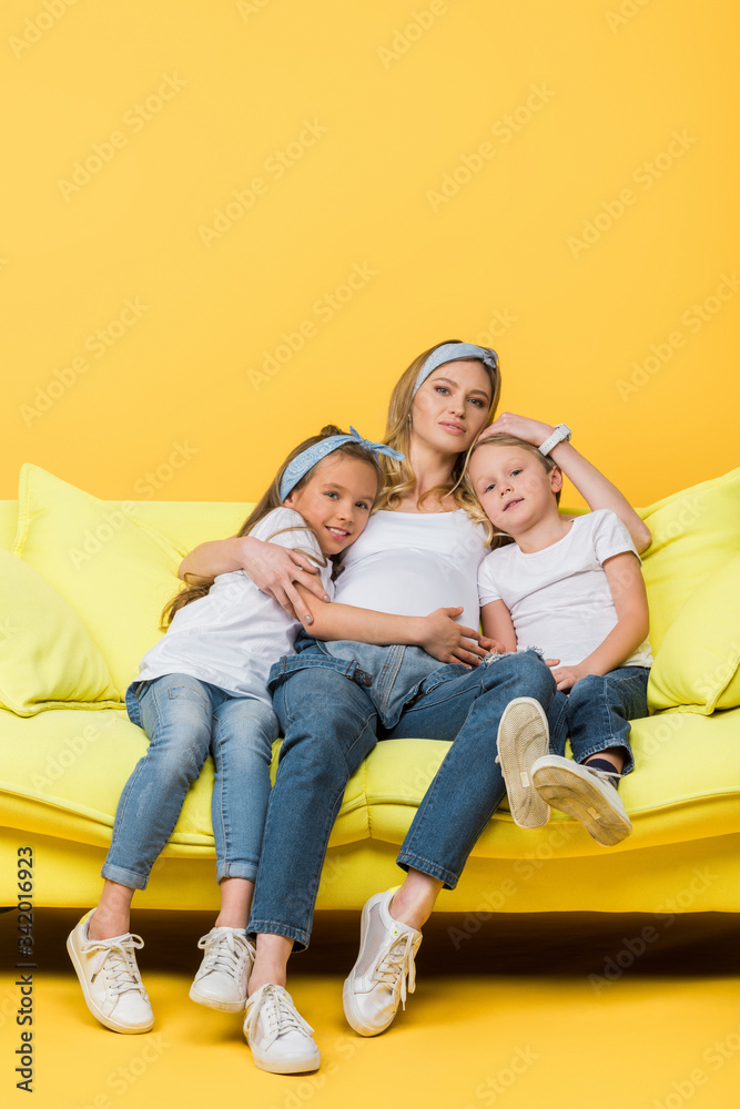 beautiful pregnant mother hugging with daughter and son on sofa on yellow