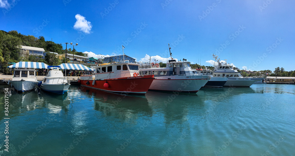 St.John/US Virgin Islands-Mar 14 2017: View at the wharf with small boats and yachts, moored near the tropical island coast. Travel natural landscape of dock with turquoise water, blue sky. Sea voyage