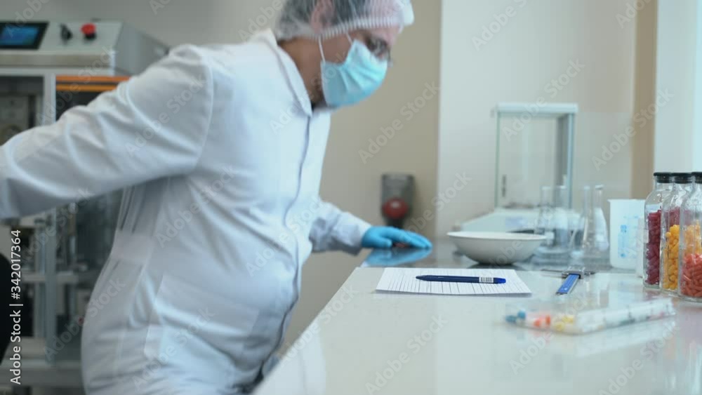 Male scientist working with medicines sitting at table in modern pharmaceutical laboratory spbas. Man employee examines new drugs for virus and writes report at desk in company. Professional wearing Male scientist working with medicines sitting at table in modern pharmaceutical laboratory spbas. Man employee examines new drugs for virus and writes report at desk in company. Professional wearing