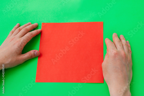 Men's hands fold a heart from red paper in the origami technique on a green background.Step-by-step instructions, step 1.Gift concept for Valentine's day, mother's day