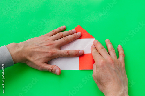  Men's hands fold a heart from red paper in the origami technique on a green background.Step-by-step instructions, step 7. Gift concept for Valentine's day, mother's day