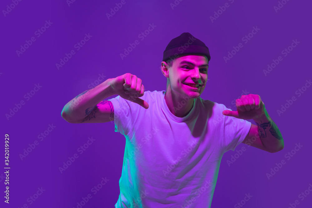 Thumbs up, pointing. Caucasian man's portrait isolated on purple studio background in pink neon light. Beautiful male model in casual. Concept of human emotions, facial expression, sales, ad. Thumbs up, pointing. Caucasian man's portrait isolated on purple studio background in pink neon light. Beautiful male model in casual. Concept of human emotions, facial expression, sales, ad.