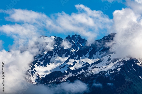 Snow capped rugged rocky mountains on blue sky day with clouds on the Kenai Peninsula of Alaska
