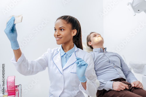 selective focus of happy african american dentist holding teeth palette near patient in clinic
