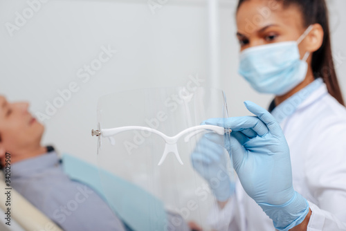 selective focus of african american dentist in medical mask holding face shield near patient