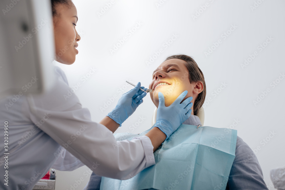 selective focus of african american dentist in latex gloves holding dental instrument near happy patient