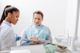 selective focus of african american dentist in latex gloves and man looking at teeth palette