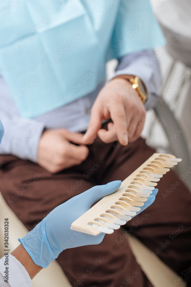 cropped view of man pointing with finger at teeth palette near dentist in latex gloves