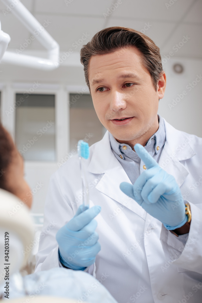 selective focus of dentist gesturing near african american woman while holding toothbrush selective focus of dentist gesturing near african american woman while holding toothbrush