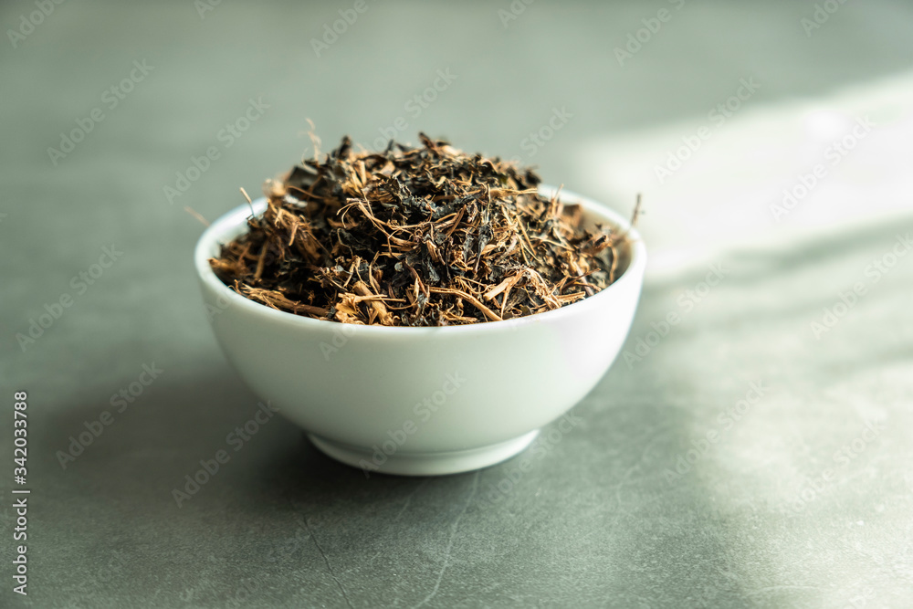 Fototapeta premium Dry black tea leaf in white porcelain bowl on concrete, stone background. Traditional, healthy and organic beverage.