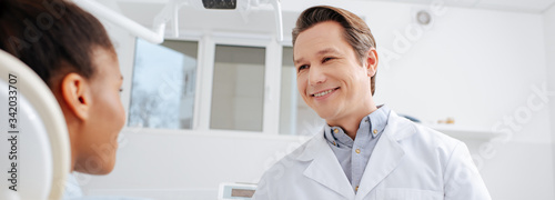 panoramic shot of happy dentist looking at african american patient