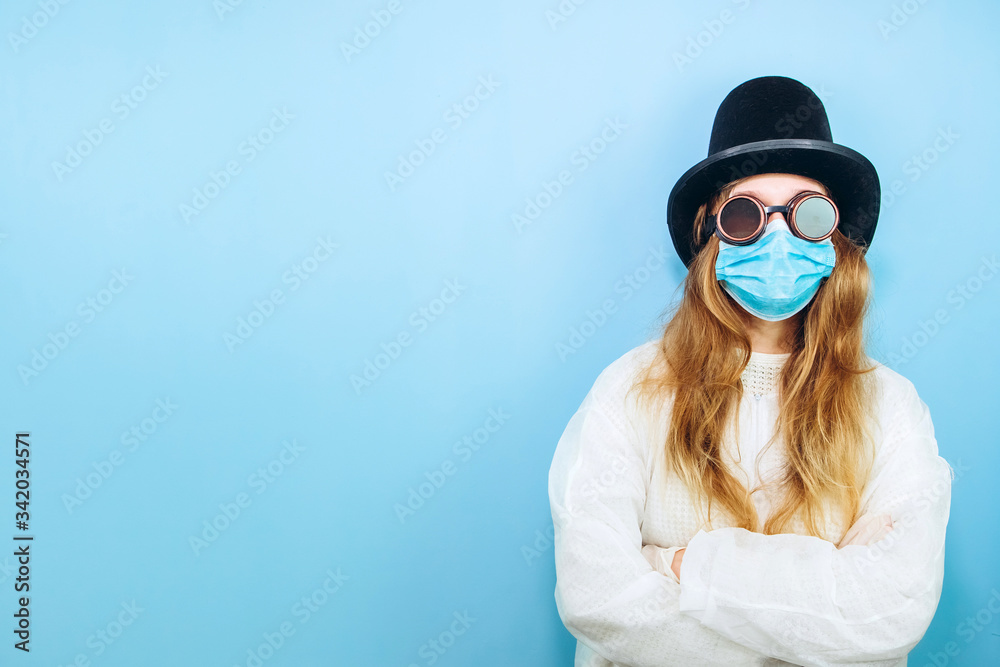 Creative girl in a white robe, medical mask, glasses and a hat on a blue background. Self-isolation during coronavirus quarantine. Epidemic covid-2019.