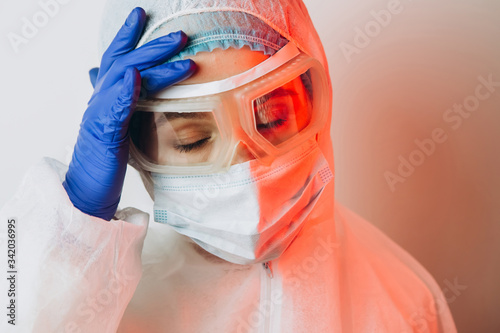 Doctor in protective uniform, reperitor, glasses, gloves on a blue background in neon light. A close-up portrait of a doctor in red neon. A tired man is battling a coronavirus. COVID 19 photo