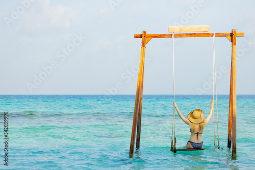 Back view of beautiful woman in vacation holidays at the beach relaxing on a swing bench in ocean , travel concept