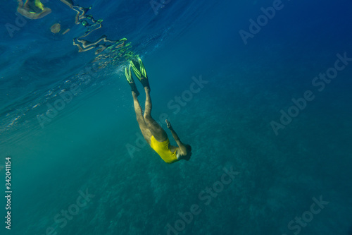 Attractive pretty girl in yellow suit dives with fins underwater over the sandy bottom in a tropical ocean. Freediving and snorkeling in Indian ocean, Maldives.