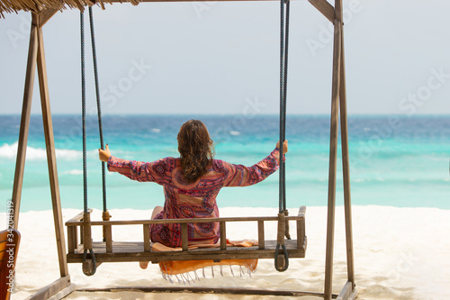 Back view of beautiful woman in vacation holidays at the beach relaxing on a swing bench near ocean coast, travel concept