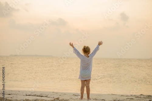 Back view of joyful cute little girl with arms up on beach is enjoying ocean sunset during summer holidays travel. Happy childhood concept © Whiteline